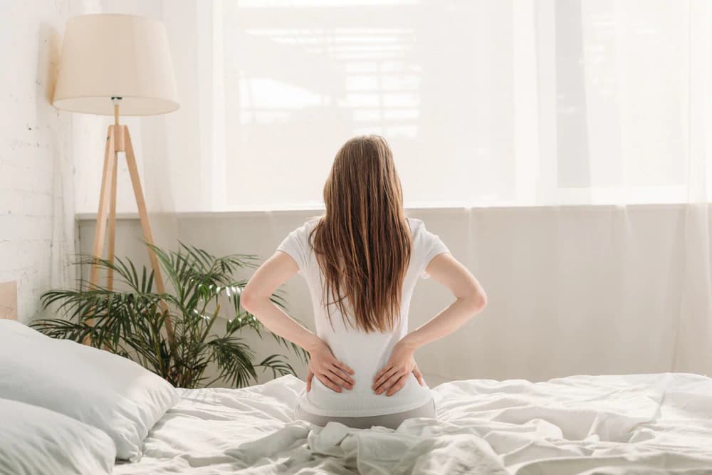 Young woman sitting on her bed holding her back
