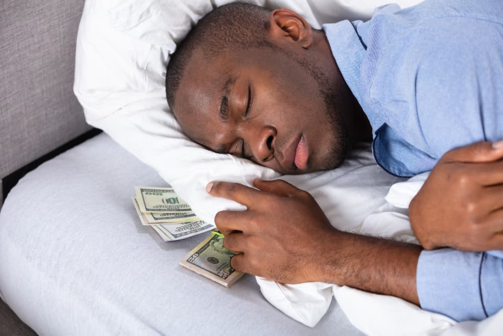 Man sleeping on mattress with dollar bills under his pillow