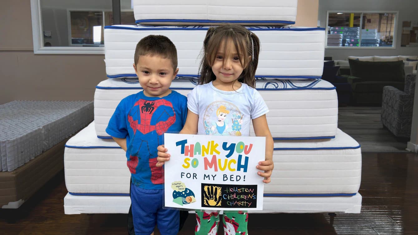 Two Houston children standing in front of mattresses with a "thank you" sign