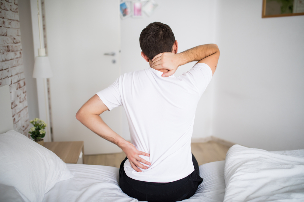 Man getting out of bed holding his neck and back.